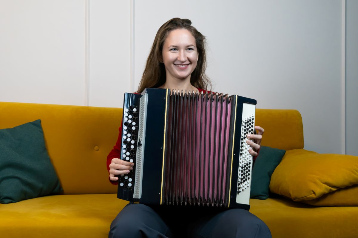 A female sitting on the couch smiling while playing the Accordion